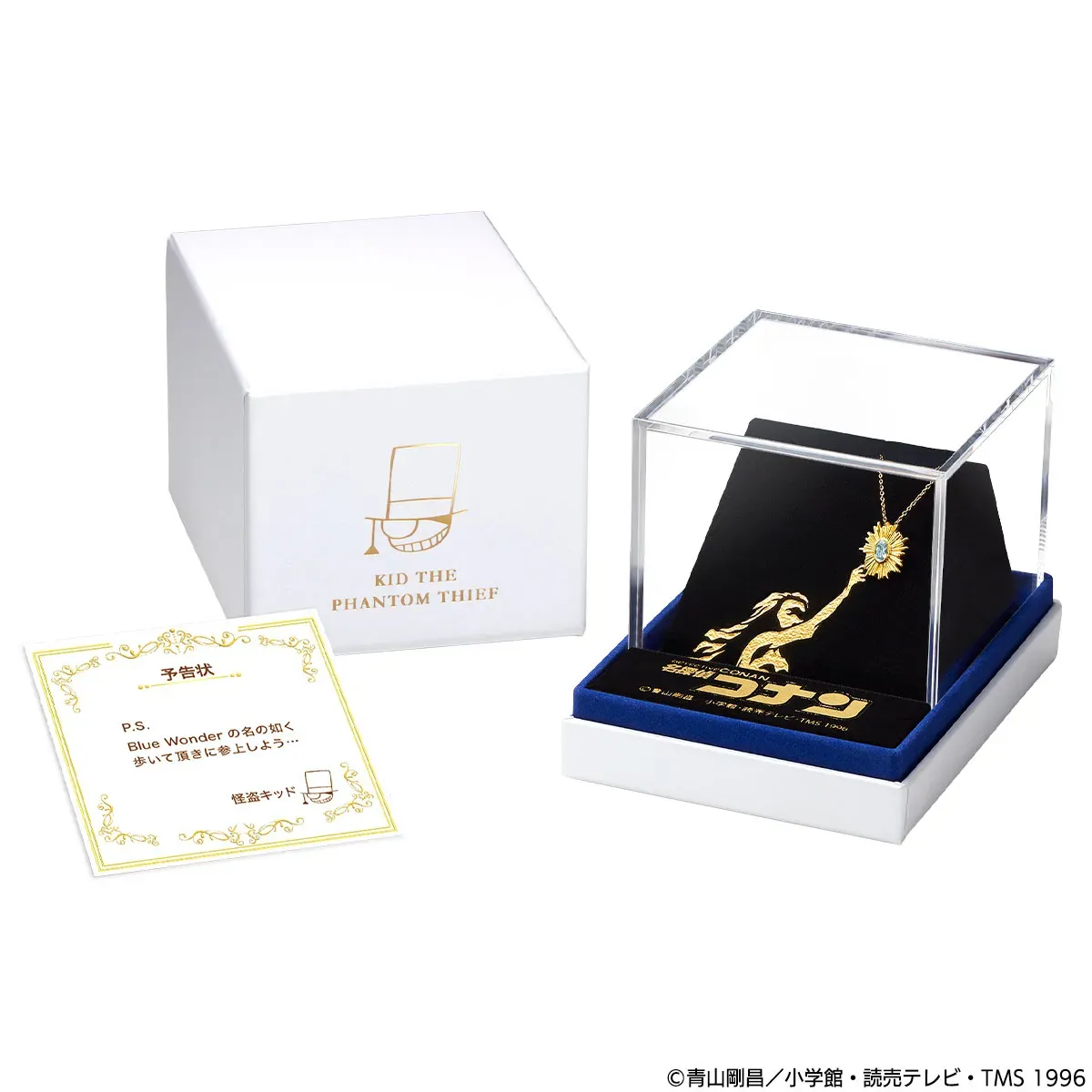 白い箱と透明なケースに入った、怪盗キッドのネックレスのセット。ネックレスは金色で、青い石が輝いている。箱には怪盗キッドのロゴが、ケースの台座には怪盗キッドのシルエットが描かれている。手前には予告状が置かれている