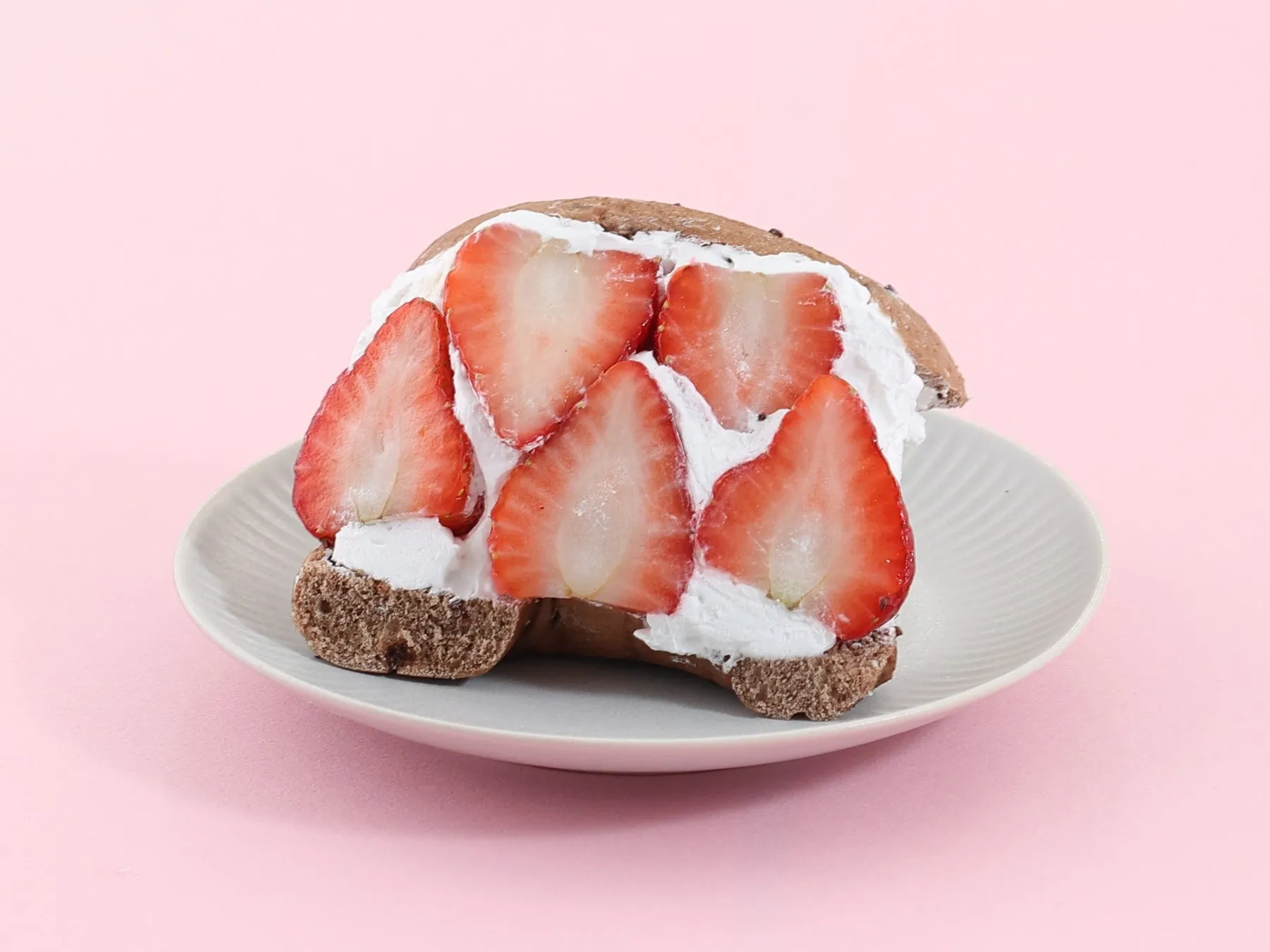 いちごが乗ったケーキが白い皿に載せられており、背景はピンク色です。