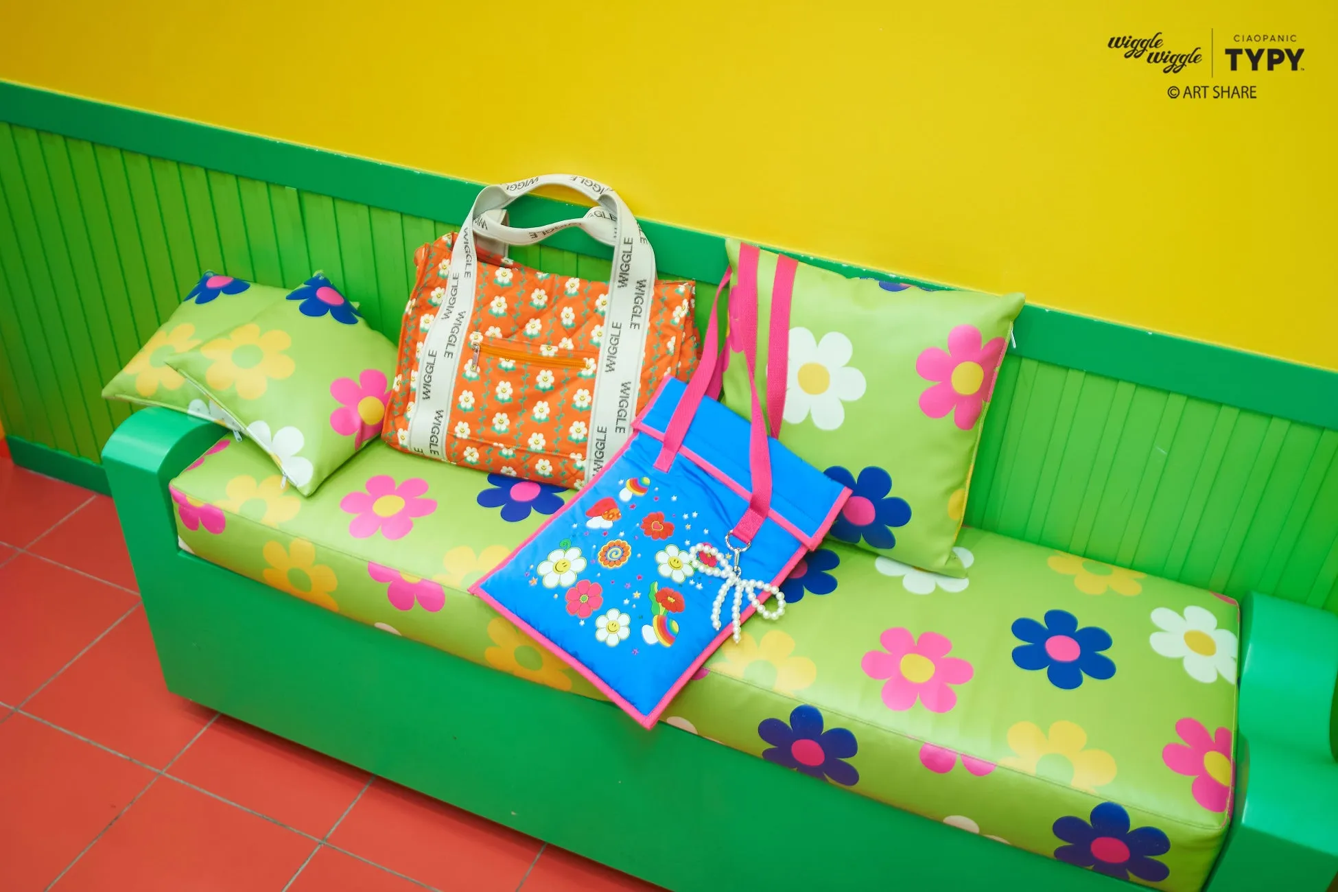 花柄のクッションとバッグが置かれたソファの写真。背景は黄色の壁と緑色の装飾。