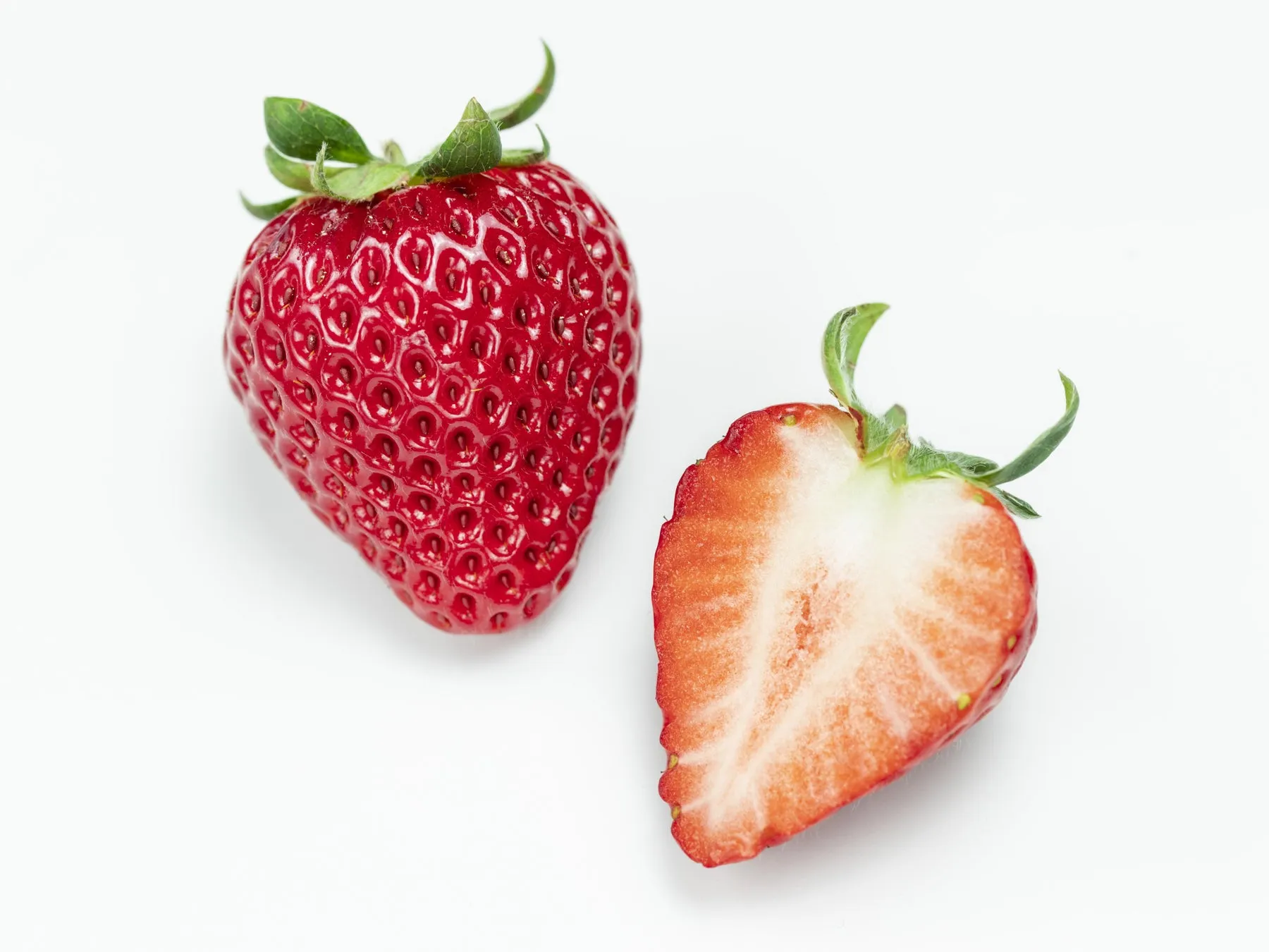 2つのイチゴが白い背景に置かれています。1つは丸ごと、もう1つは半分にカットされています。
