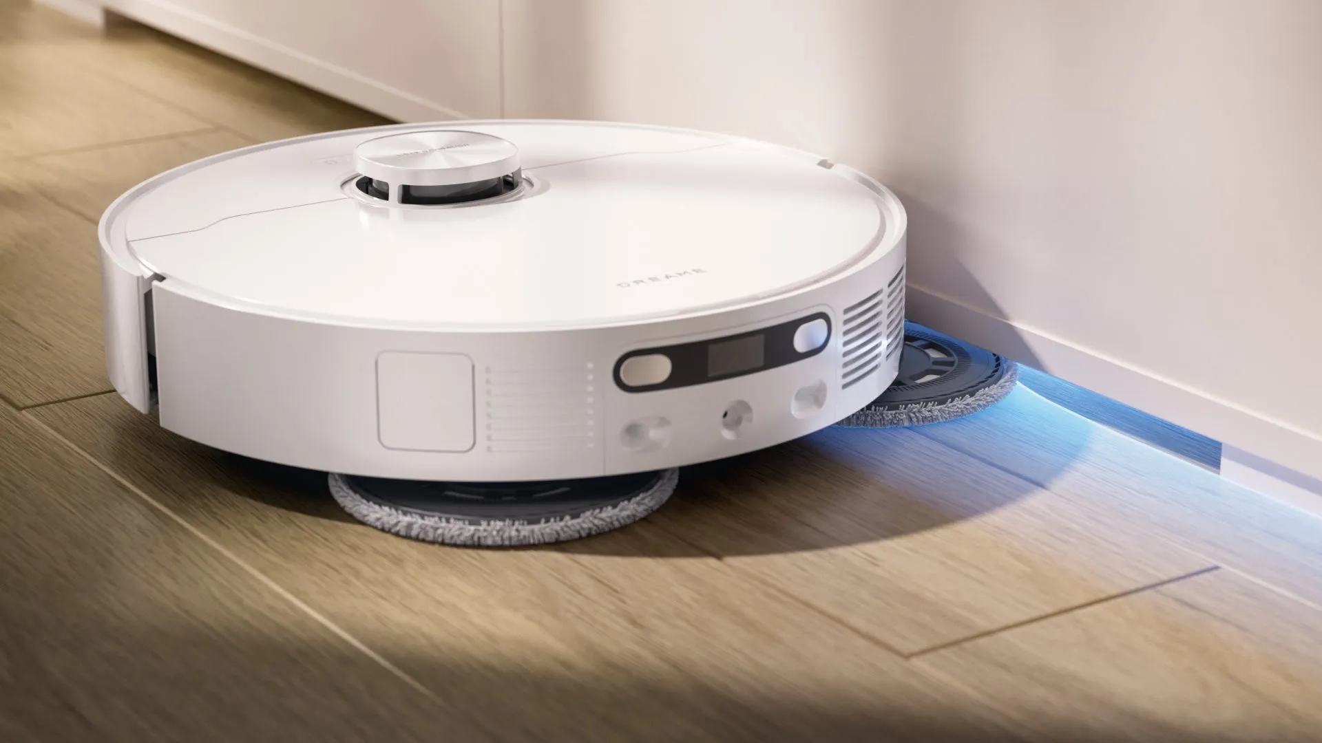 白くて丸いロボット掃除機が木製の床を掃除している様子。掃除機は壁に沿って動き、床の隙間を掃除している。