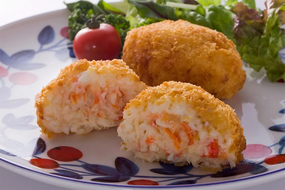 揚げられたカニクリームコロッケが3つ、サラダ、トマトが盛られたお皿の写真です。