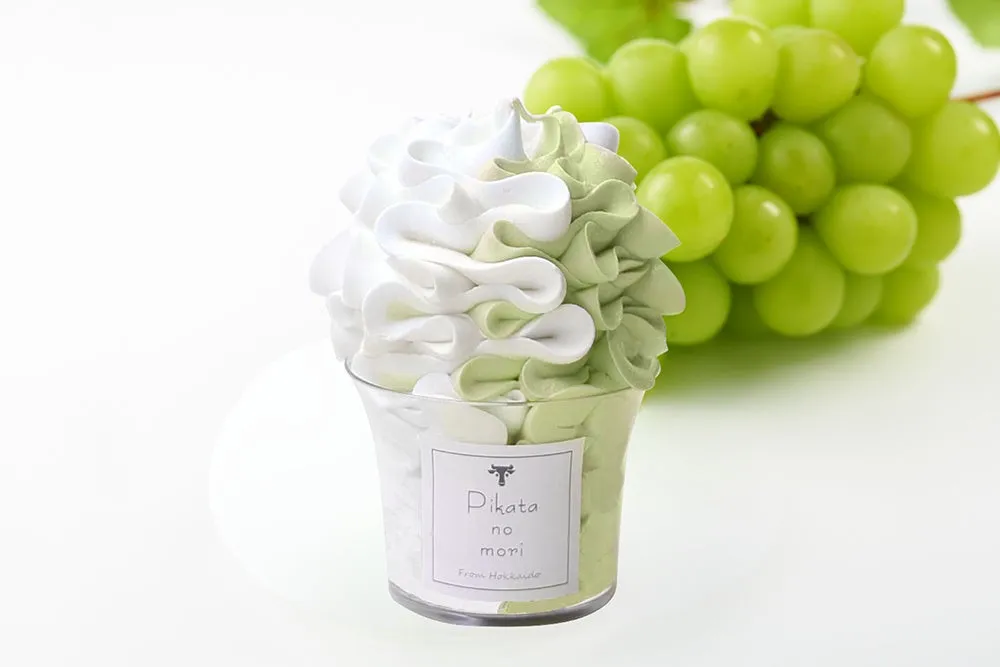 透明な容器に入った、白と緑のグラデーションが美しいデザート。背景には、新鮮なシャインマスカットが添えられています。
