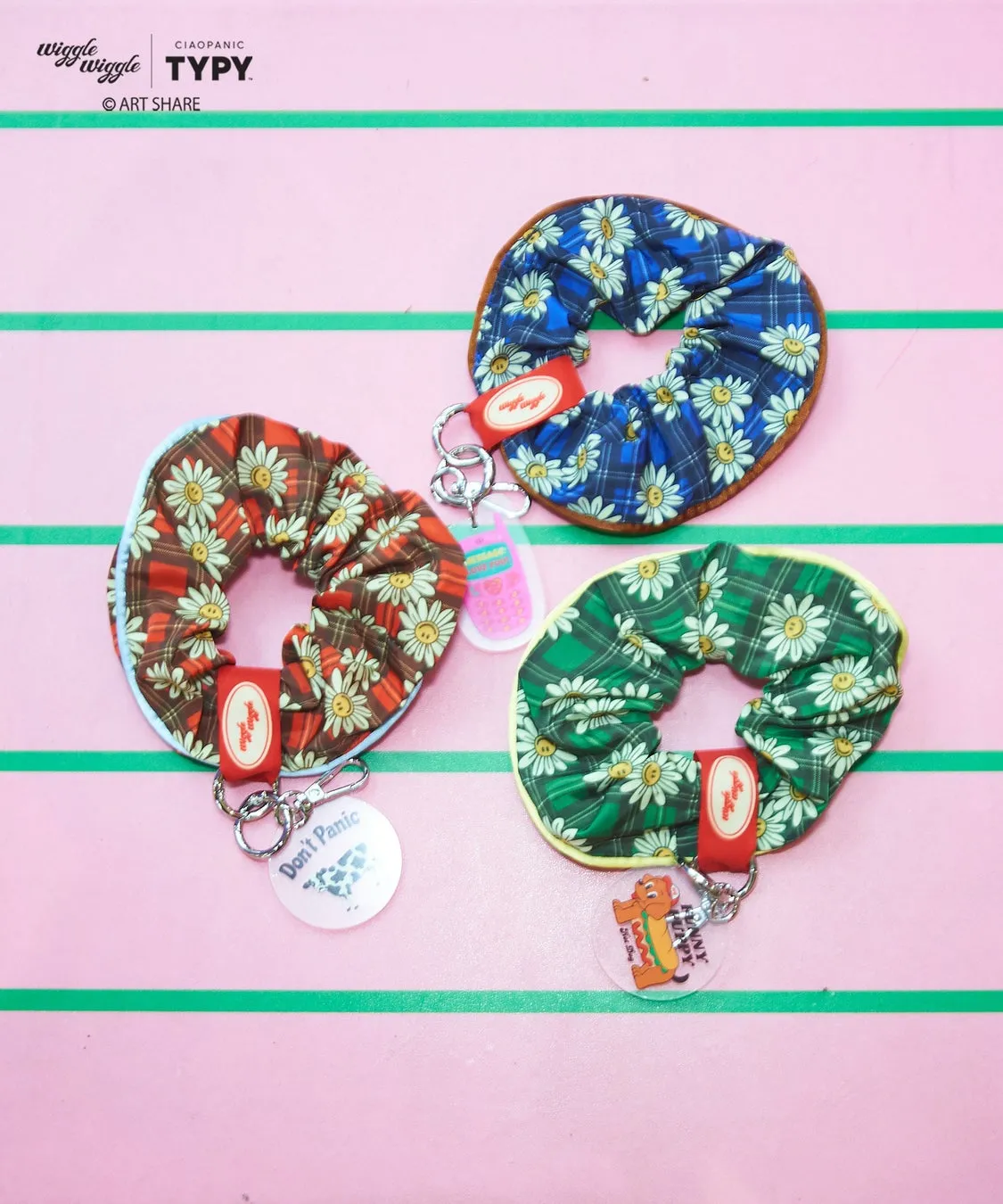 ピンク色の背景に、花柄のシュシュが3つ並んでいる写真です。シュシュにはそれぞれ、キーホルダーが付いています。