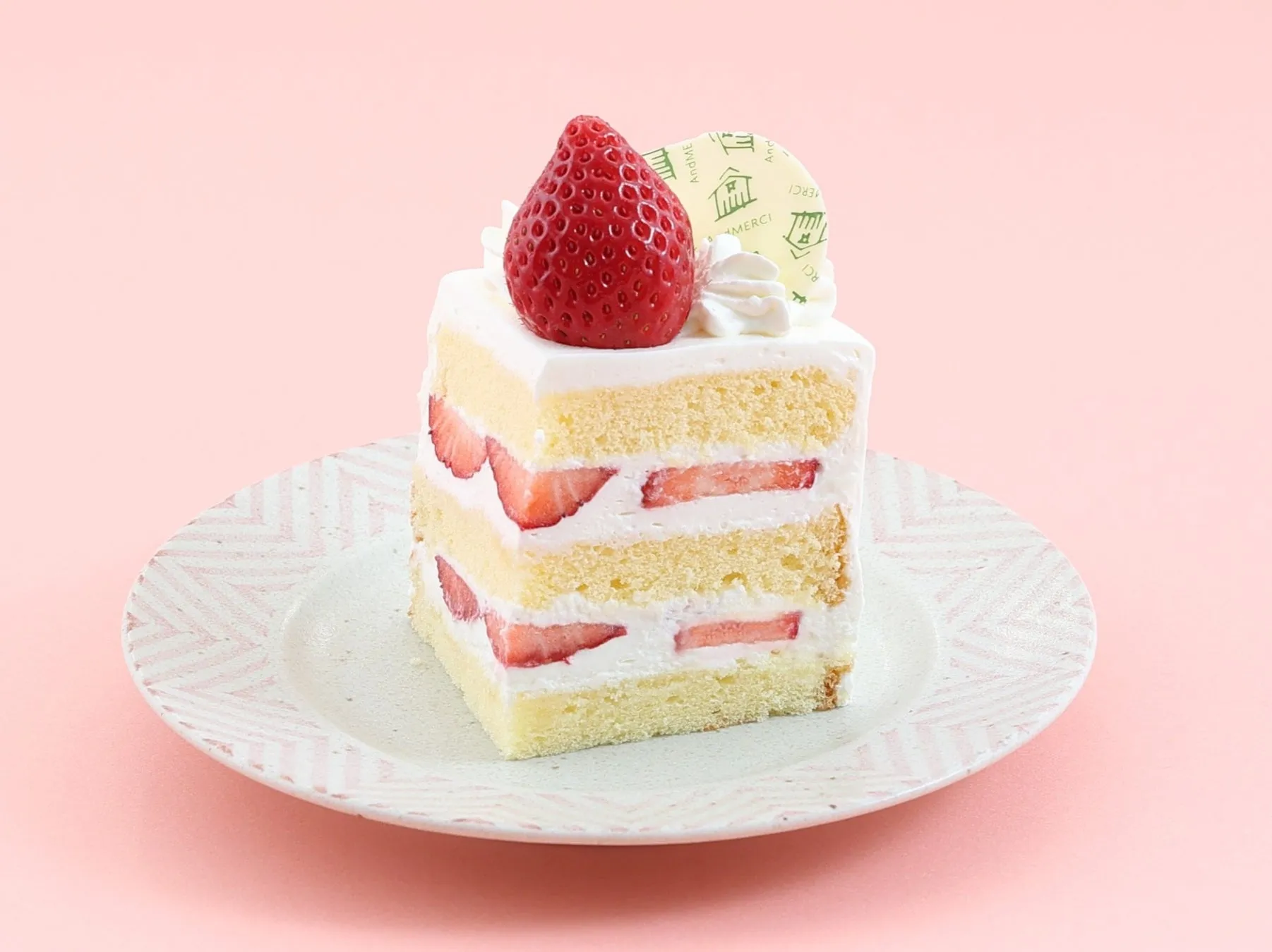 いちごがトッピングされたショートケーキの画像です。ケーキは白いクリームとスポンジで層になっており、その間にはいちごが挟まれています。ケーキは白いお皿の上に置かれており、背景はピンク色です。