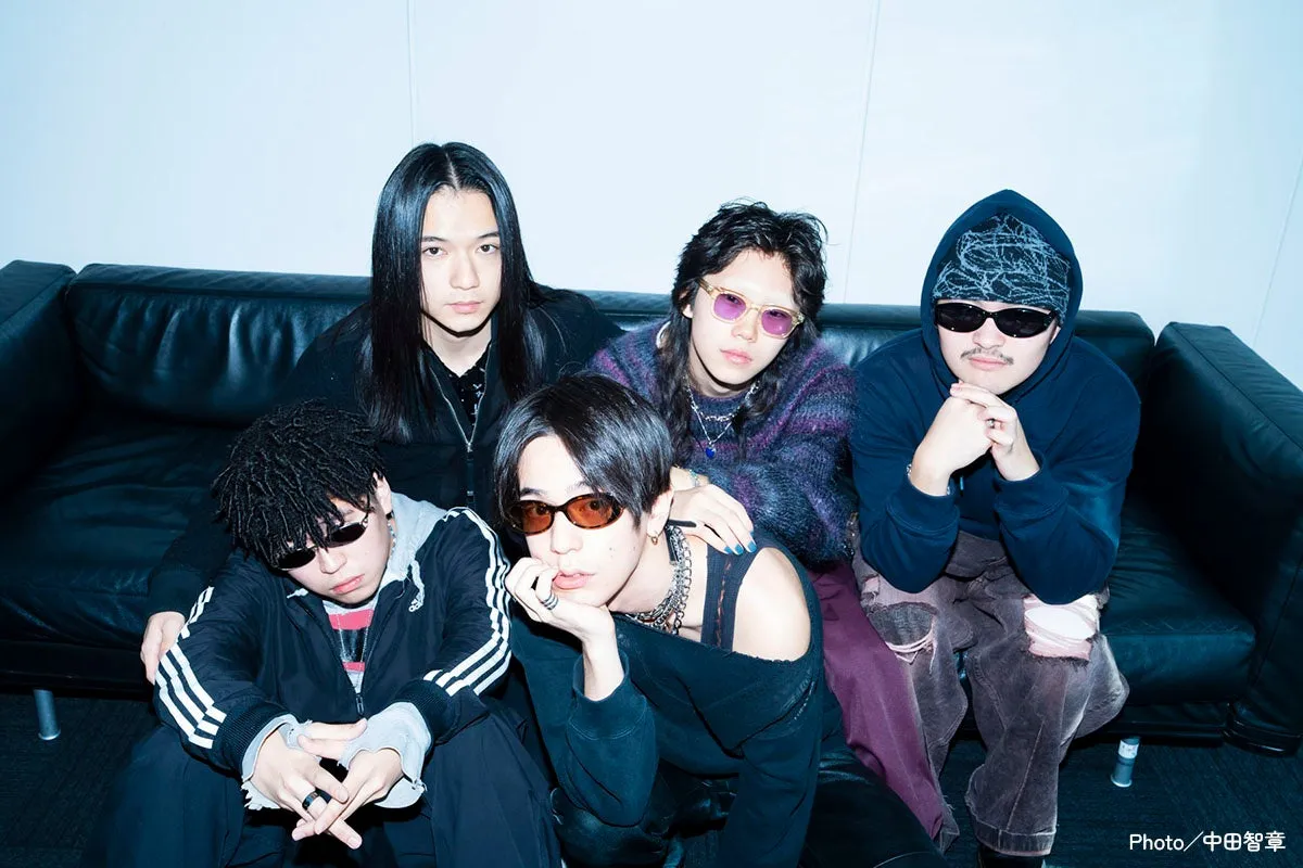 5人の男性が黒いソファに座ってポーズをとっている写真。彼らは皆、サングラスをかけており、さまざまなファッションスタイルをしています。