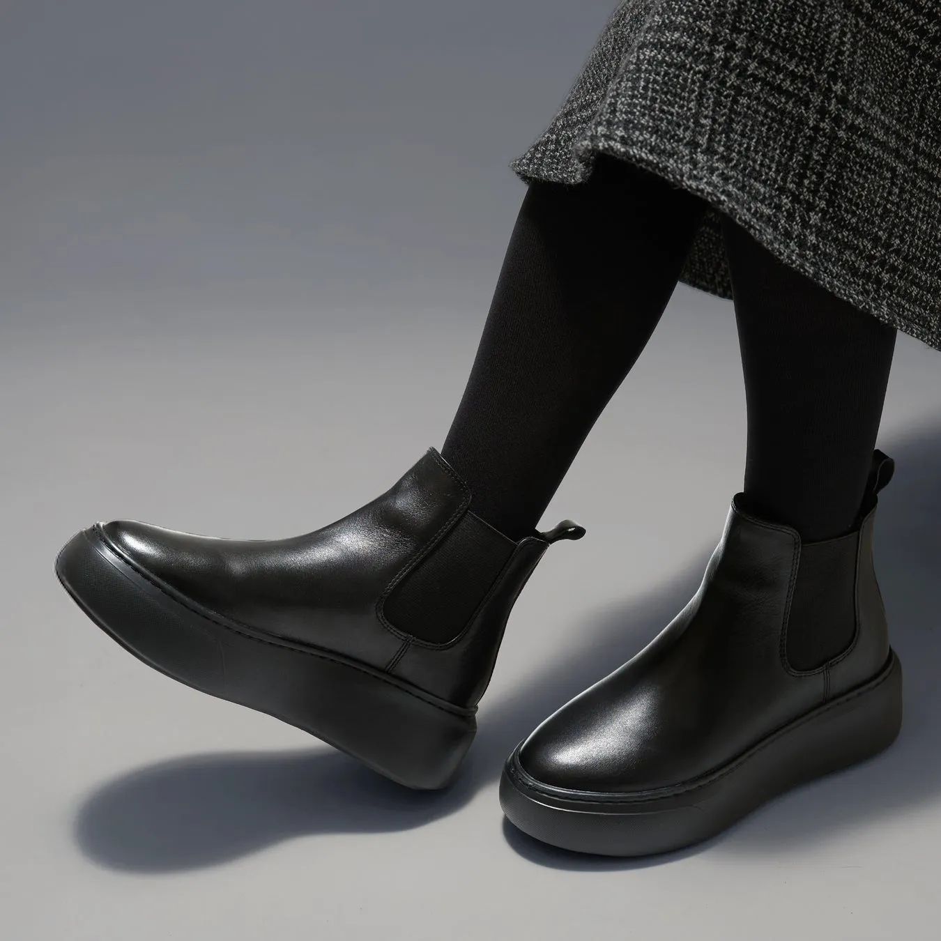 黒い革のチェルシーブーツを履いた人物のクローズアップ、チェック柄スカート