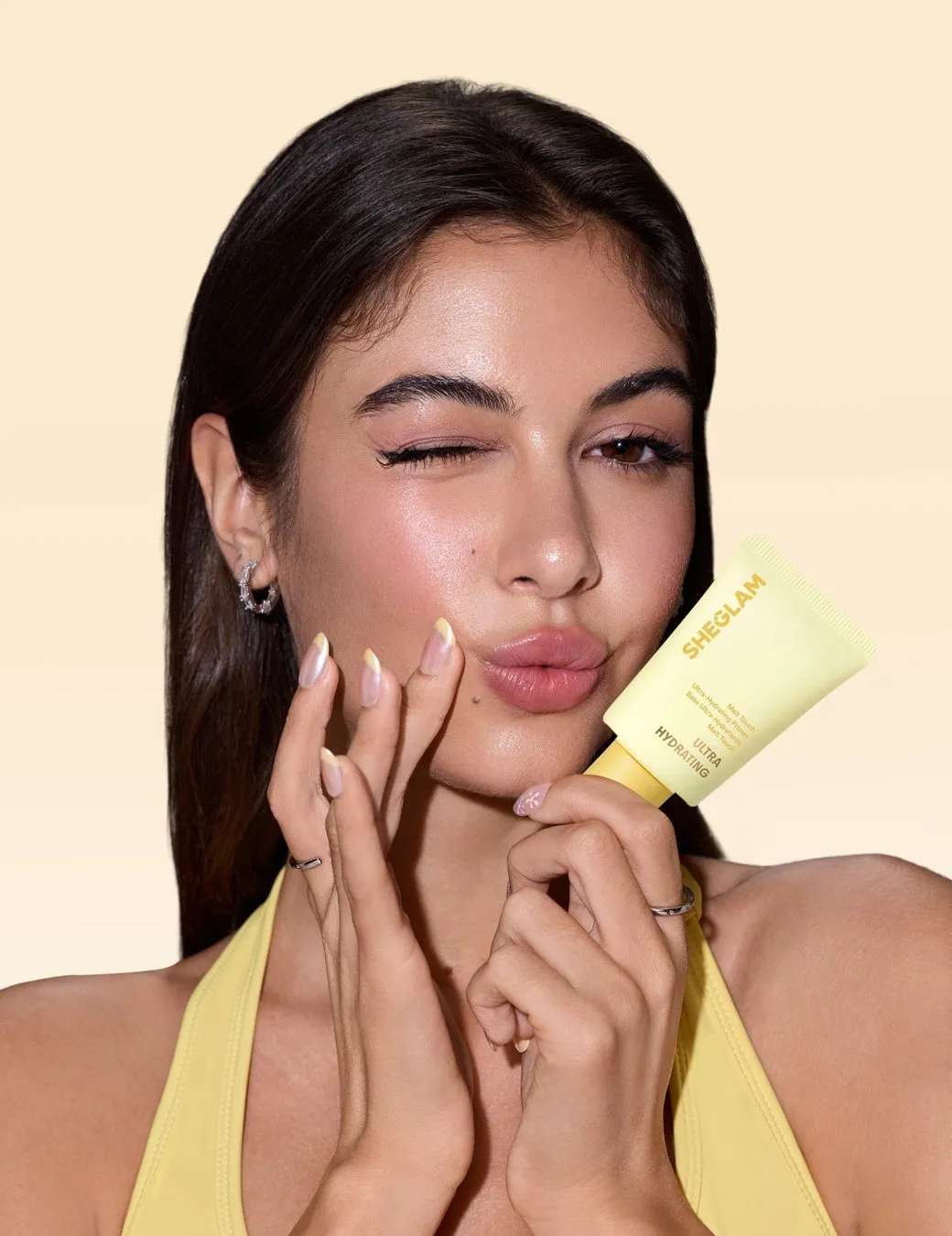 女性がSheglamのウルトラハイドレイティングプライマーを持ってウインクをしている写真