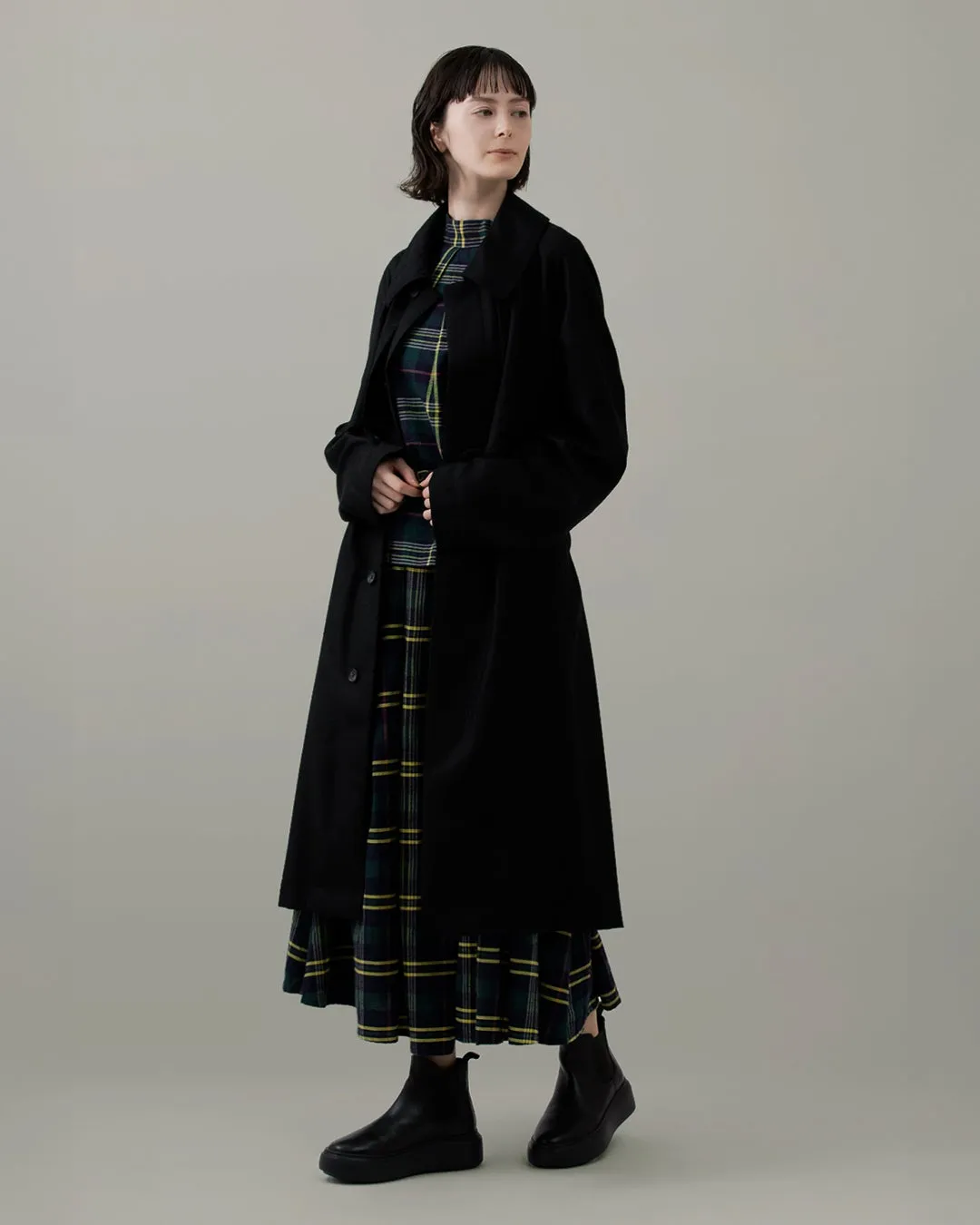 黒いコートを着た女性、チェック柄ワンピース、ブーツ