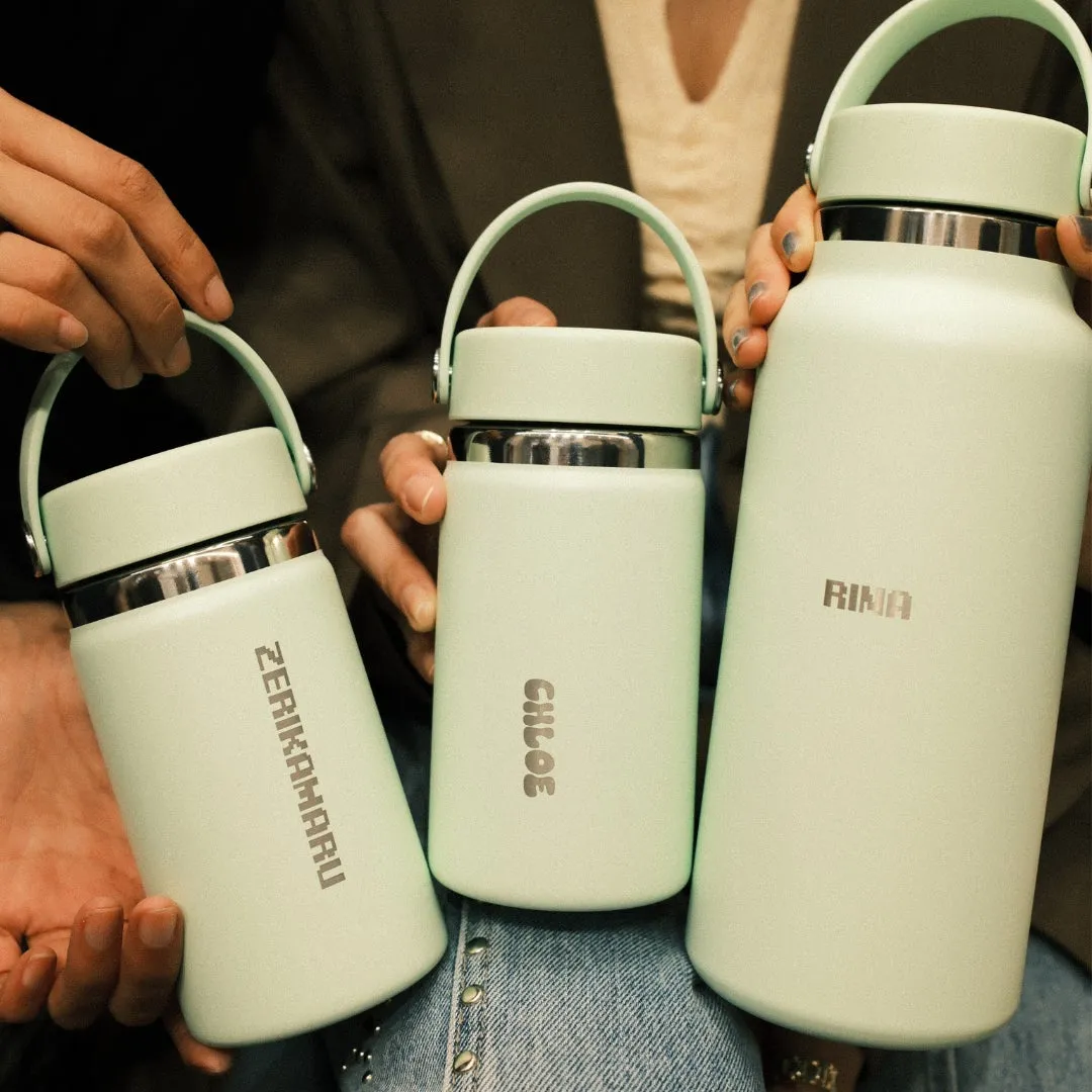 3つの水筒が並んでおり、それぞれ異なる名前が刻まれています。水筒はすべて同じデザインで、ミントグリーン色で統一されています。水筒は誰かの手によって持たれており、背景にはデニムパンツや服が見えます。