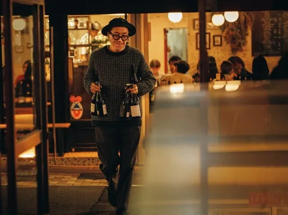 男性がワインボトルを持ってレストランから出てくる様子。