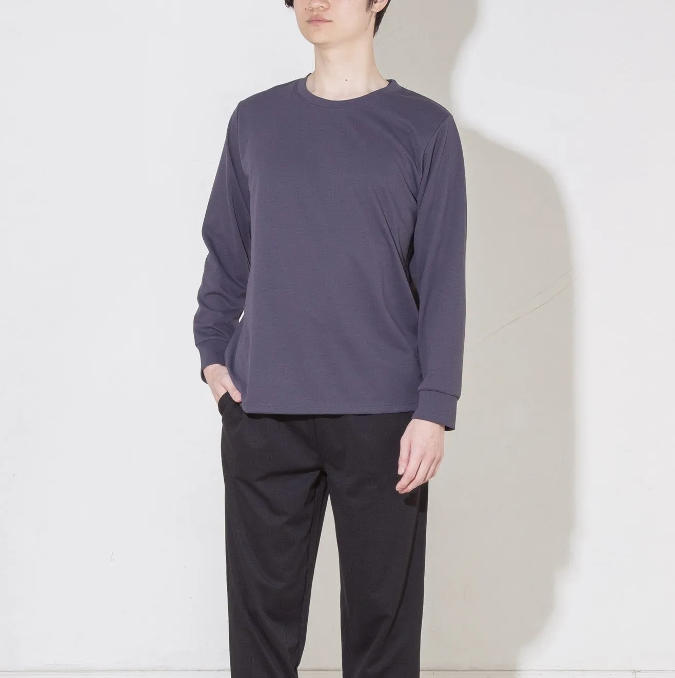 長袖Tシャツと黒いズボンを着用した男性が立っている写真です。