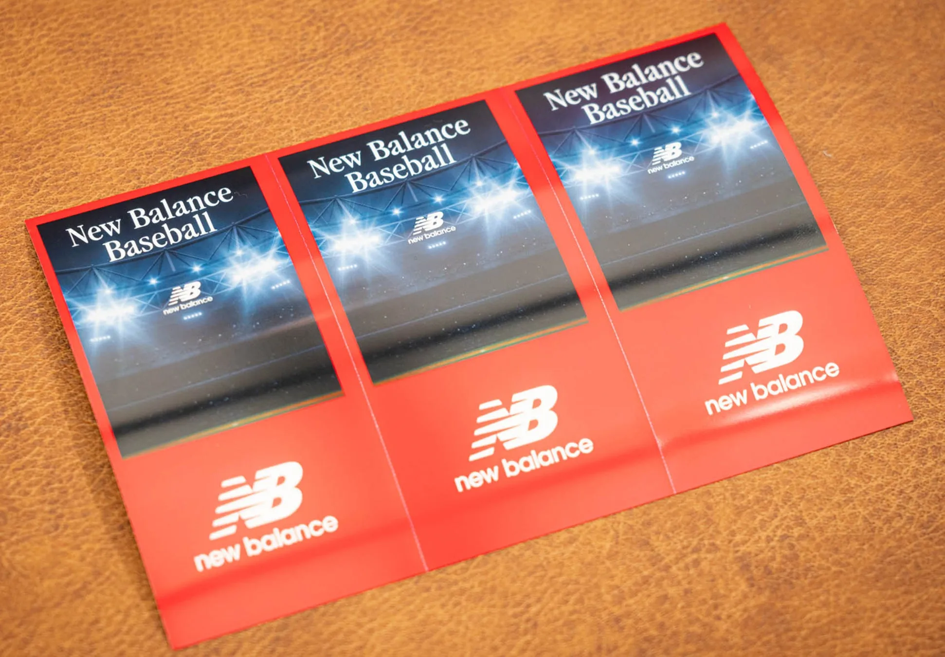 ニューバランスの野球関連の広告。赤色の紙に、スタジアムの照明とニューバランスのロゴがデザインされています。