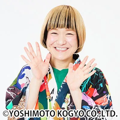 女性が両手を広げて笑顔で写っている写真です。彼女は明るい髪型をしており、カラフルな服を着ています。