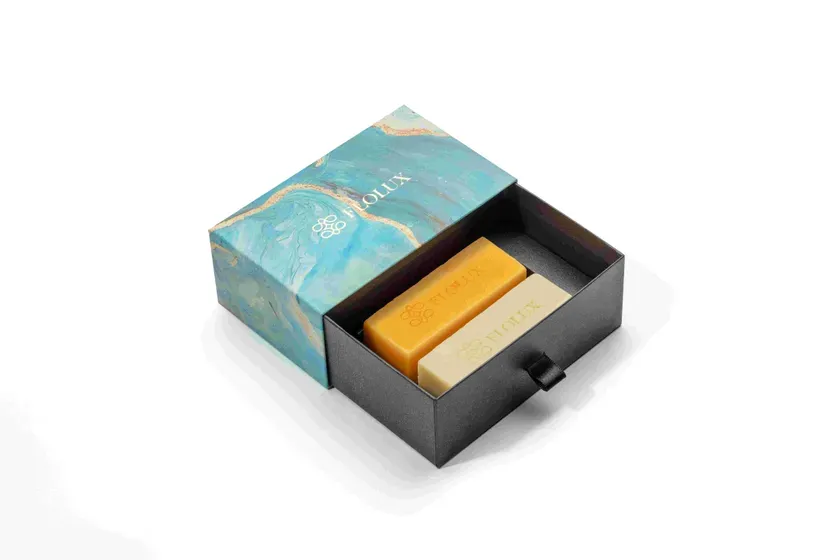 石鹸の入った箱の写真。箱は黒色で、蓋は青と白の大理石模様。石鹸は黄色と白色の2つ。