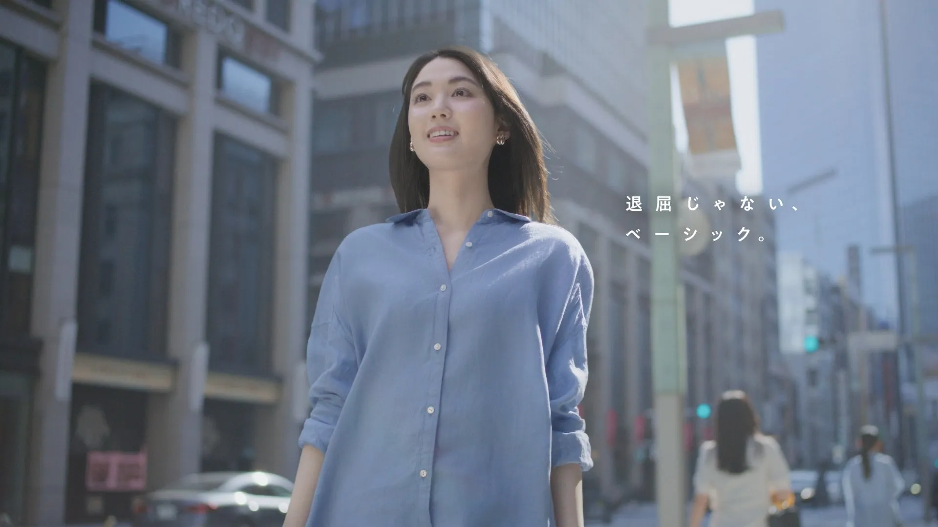 街中を歩く女性が写った広告写真。水色のシャツを着ていて、明るい表情をしている。