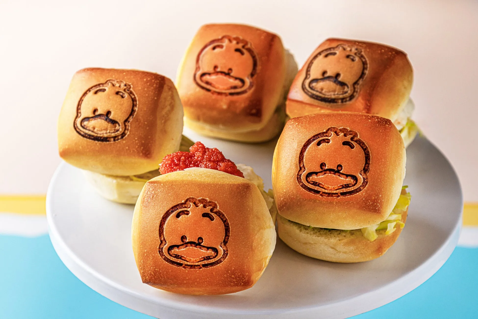 アヒルの顔が描かれたバンズのミニバーガーが、白い皿の上に並べられています。